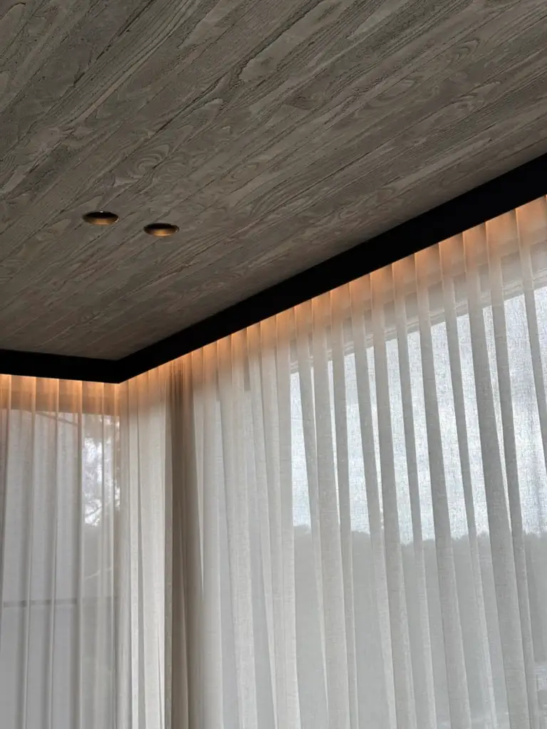 Board-marked concrete ceiling above sheer curtains with concealed perimeter lighting
