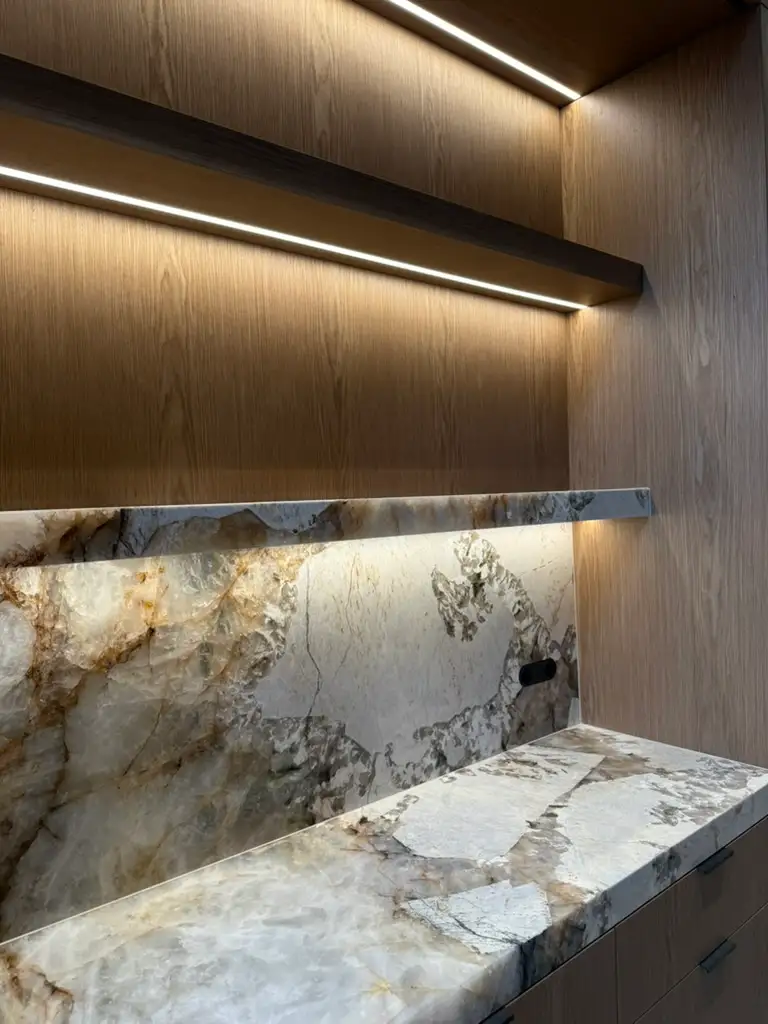 Marble kitchen splashback and worktop beneath timber shelves with concealed linear lighting