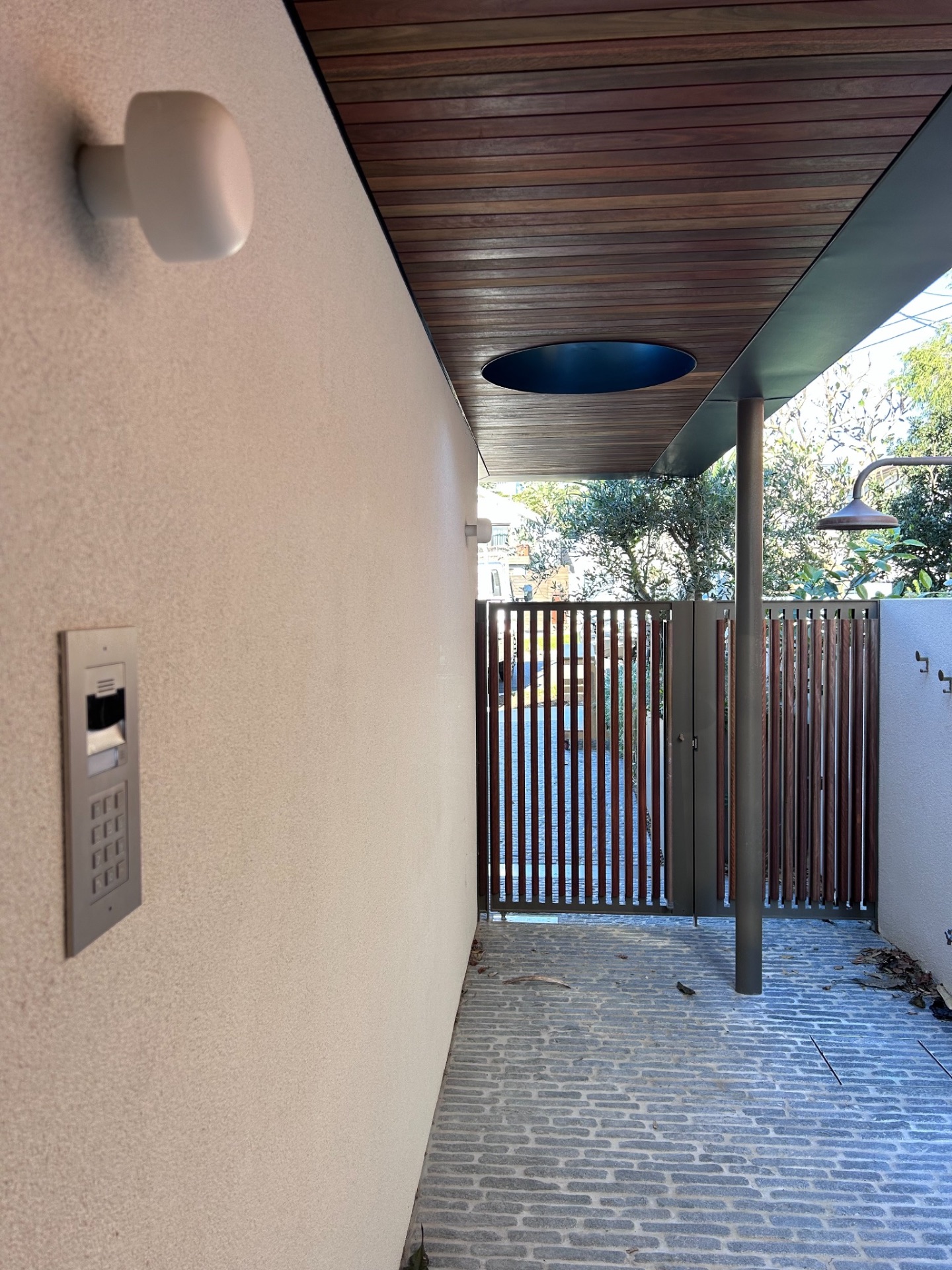 Entry with door station intercom and keypad beside a timber batten gate