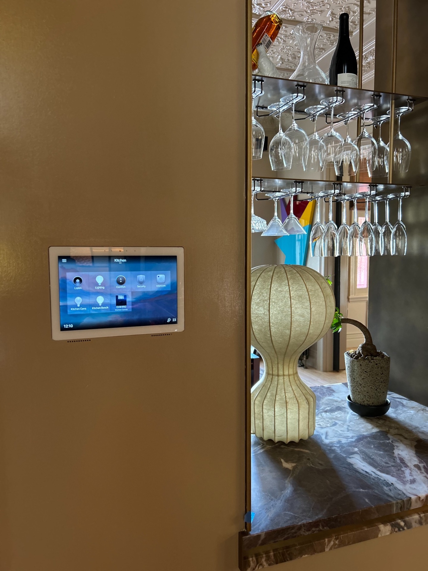 Wall mounted Control4 touchscreen beside the kitchen bar showing listen, lighting, comfort, security and intercom