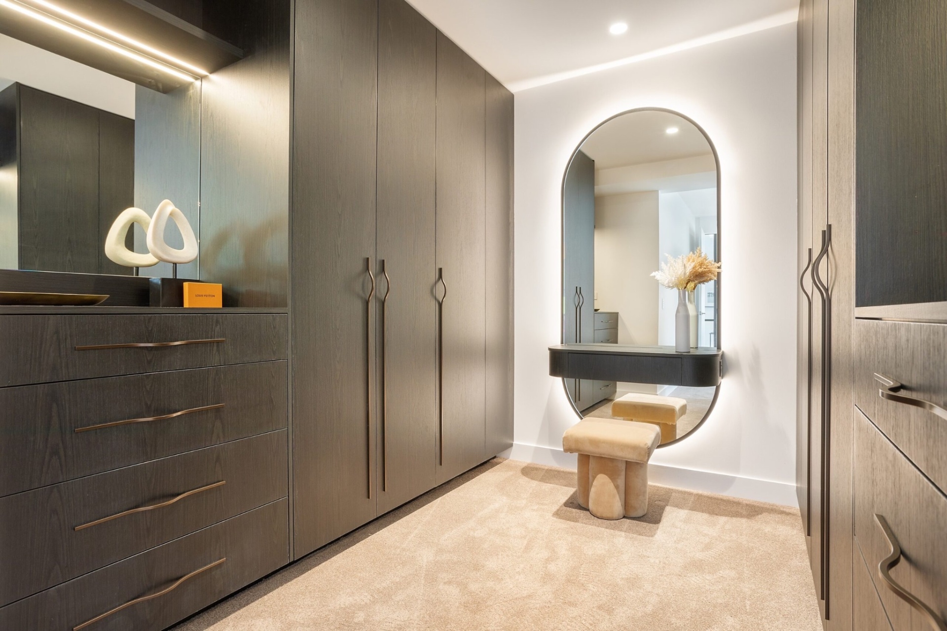 Dressing room with dark timber joinery, backlit mirror and concealed linear lighting
